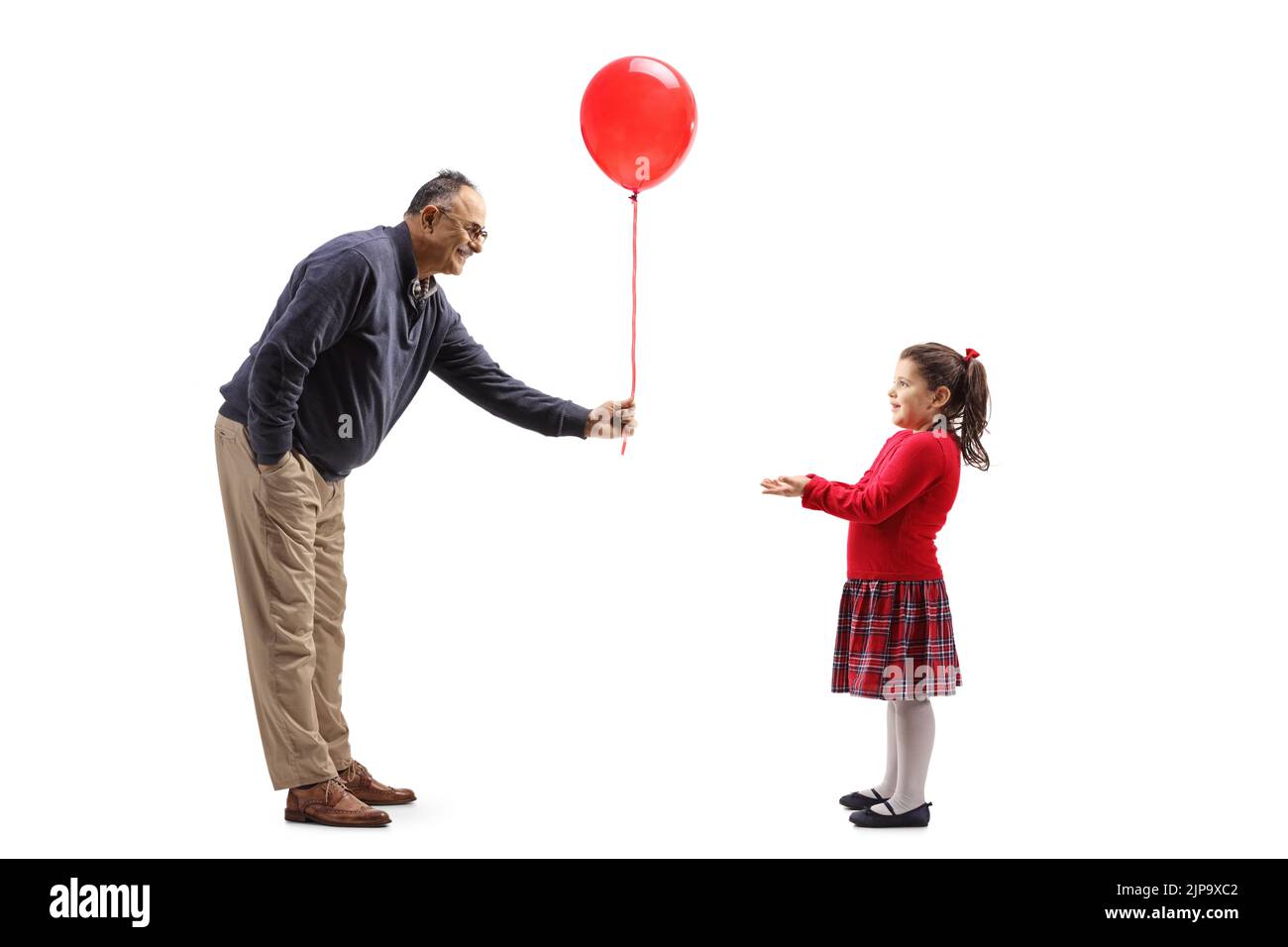 Full length profile shot of a mature man giving a red balloon to a little girl isolated on white background Stock Photo