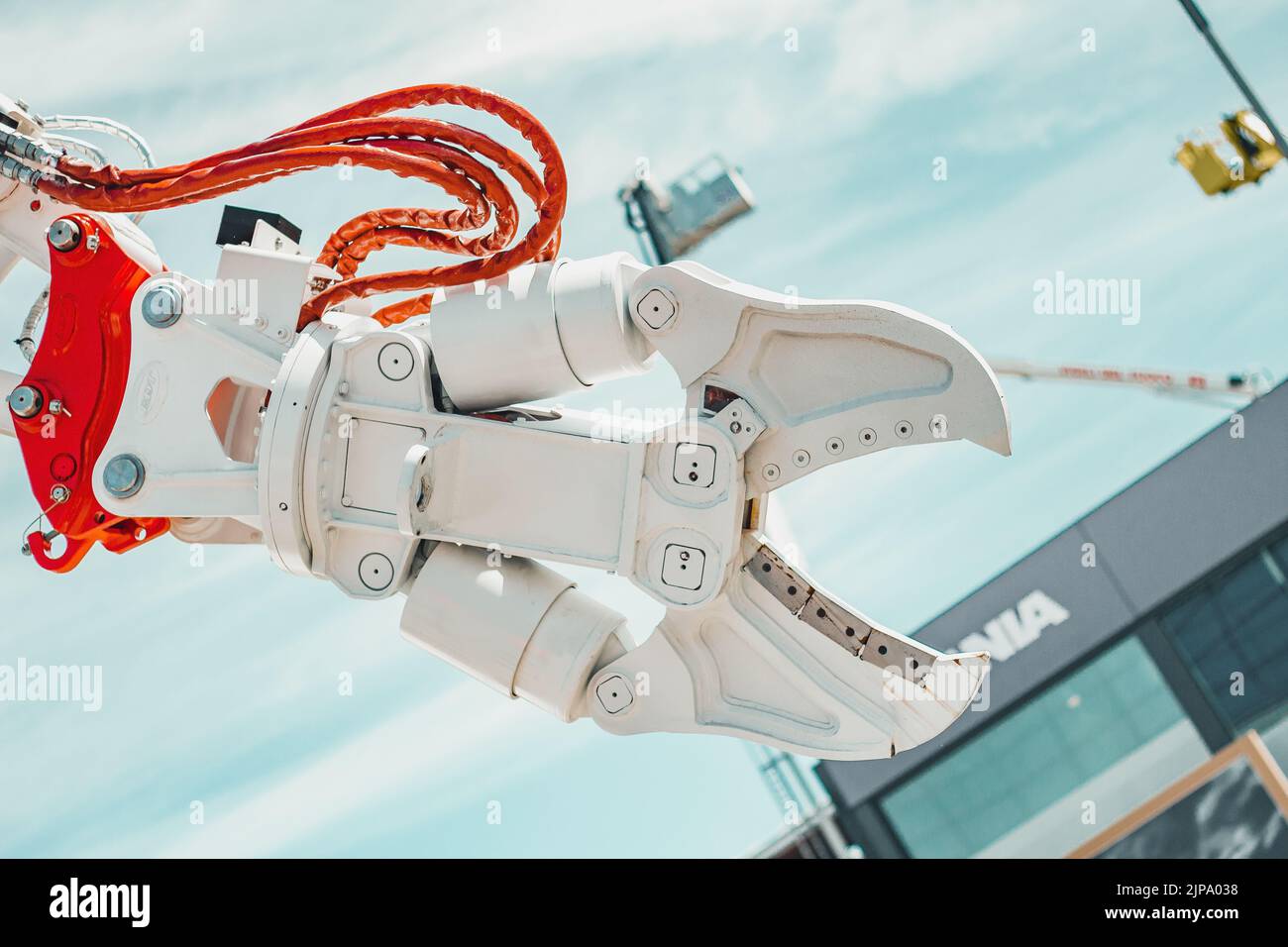 White open robotic arm with orange and red details over a blue sky and a bulding Stock Photo