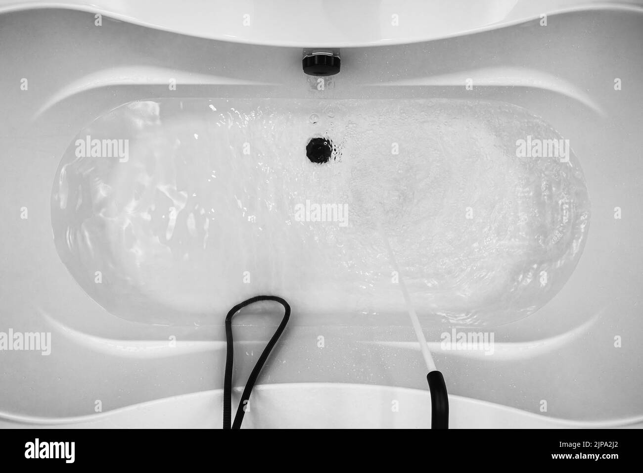 A white modern bathtub is filled with transparent water from a black faucet. Interior and design backgrounds and themes Stock Photo