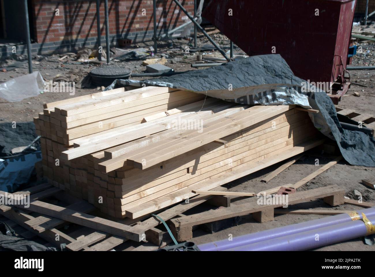 Stack of planks of wood in front of partially constructed house surrounded by scaffolding on building site Stock Photo
