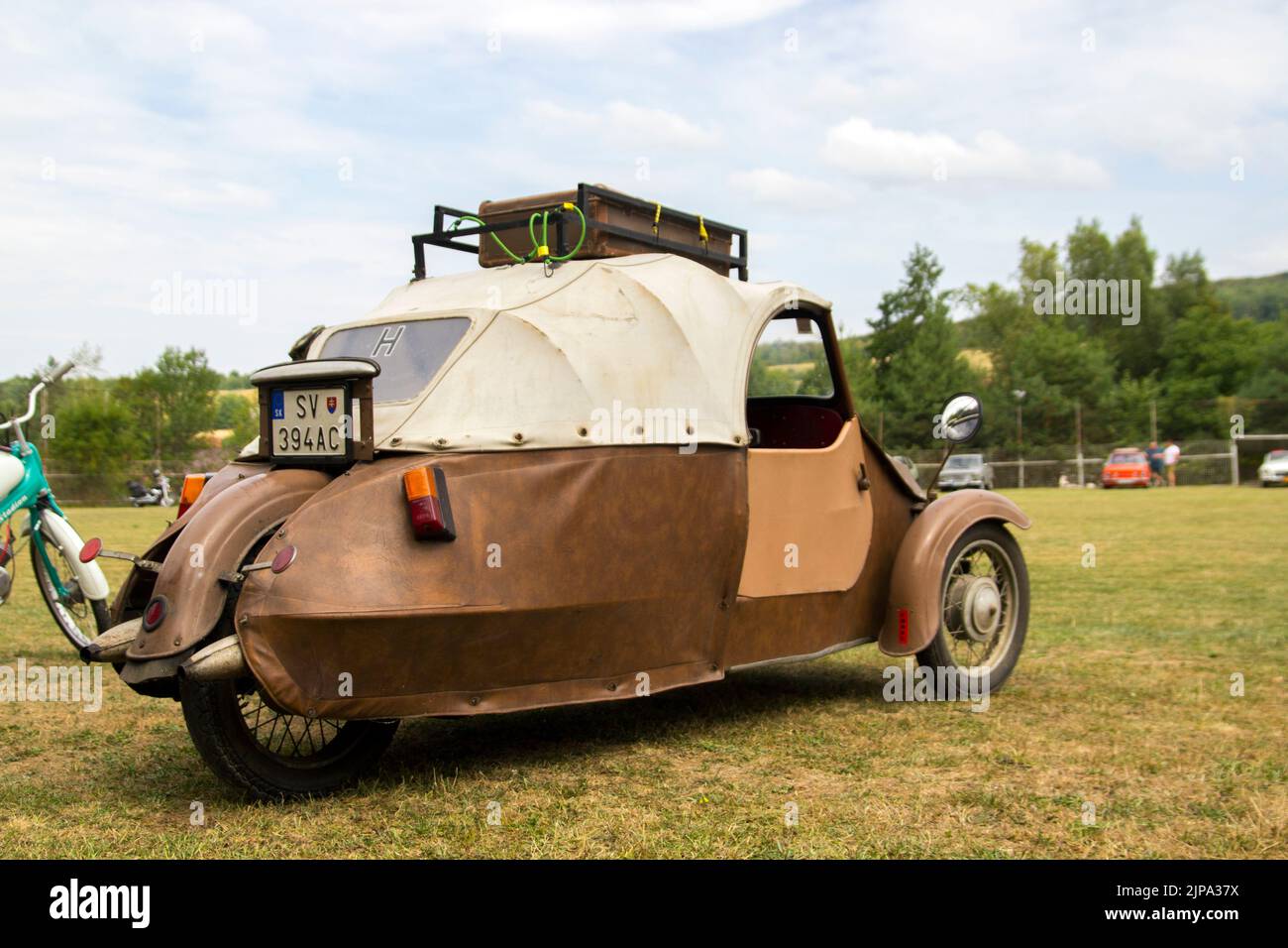 Rear Side View of Original Classic Brown Three Wheeled Leather Cloth Velorex Car with a Roof Rack at Oldtimer Classic Car Meeting Stock Photo
