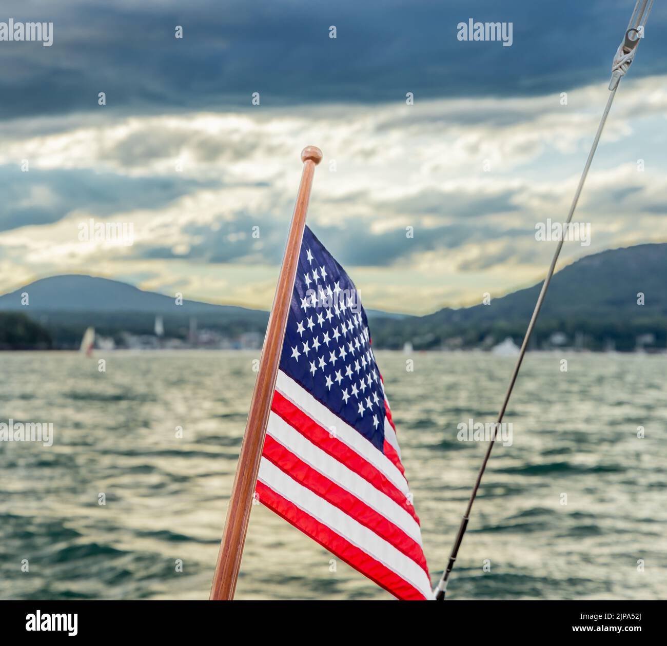 An American flag on the stern of a sail boat with a distant Camden Maine in the background Stock Photo