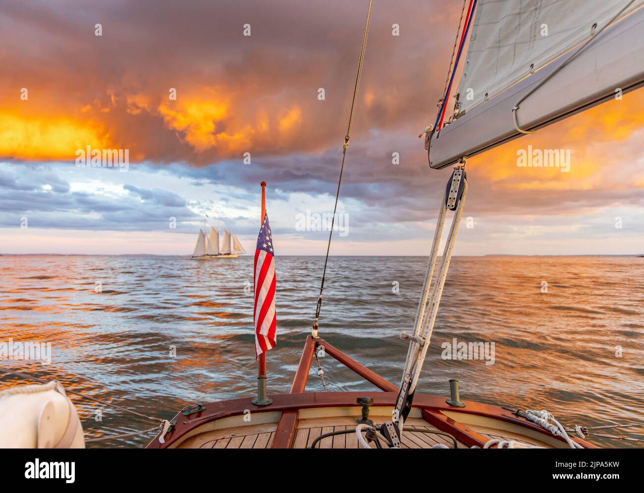 Sailing on a small sailboat with view of an incredible sunset and distant sail boat Stock Photo