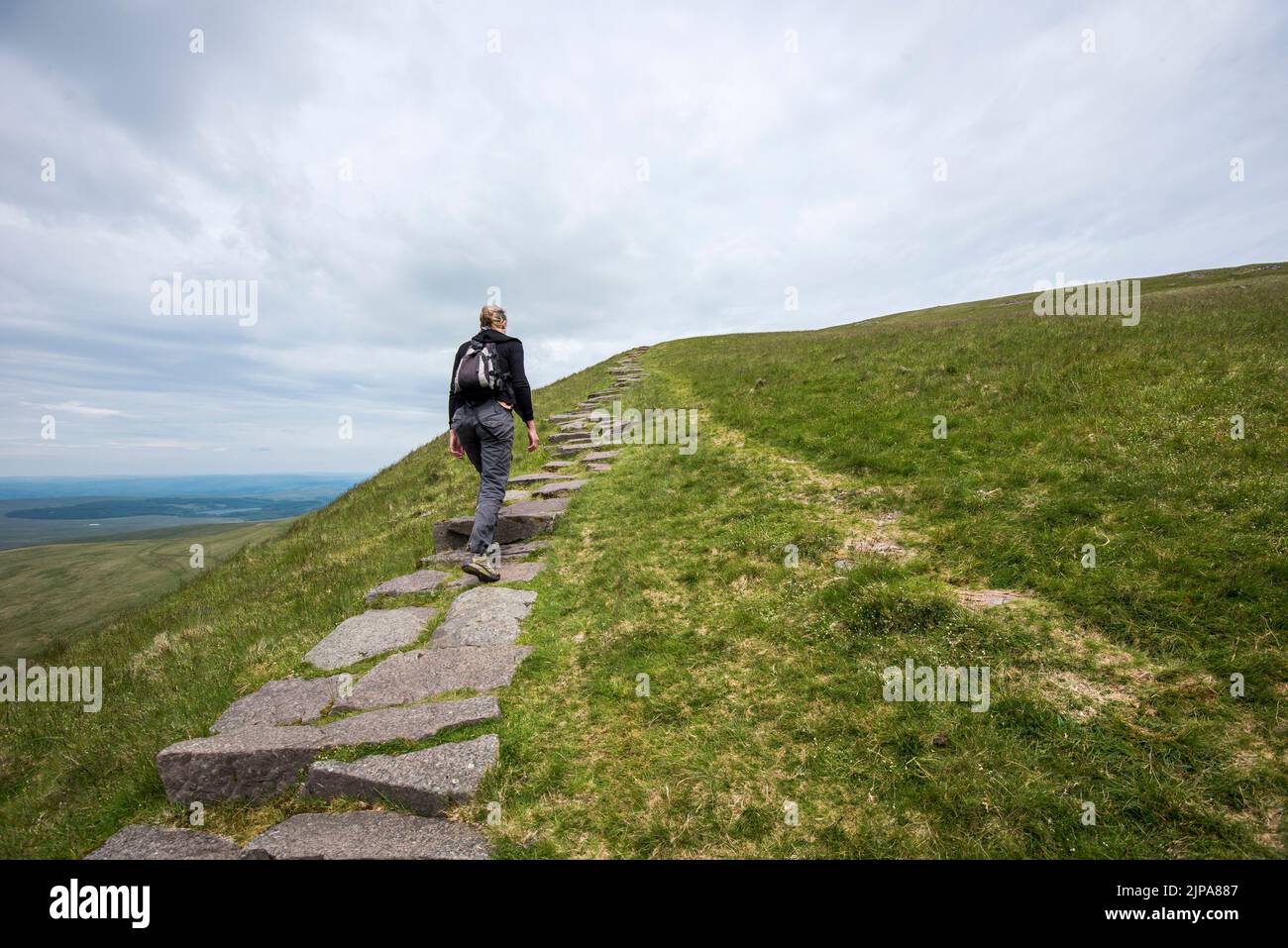 A person in a small backpack climbs stone steps in the Brecon Beacons in Wales UK Stock Photo