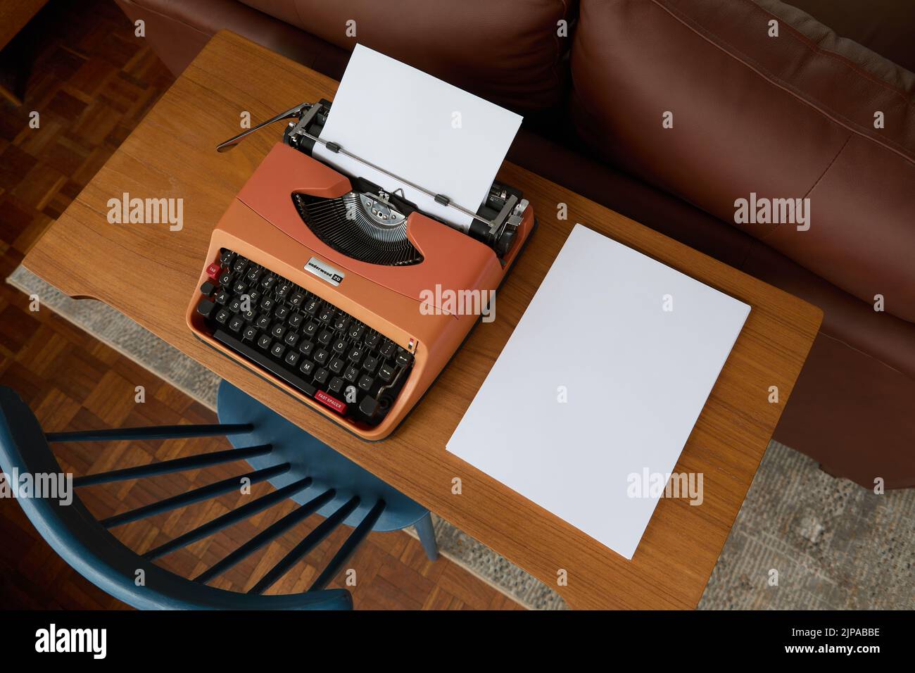 Photograph from above of a 1970's Underwood 20 typewriter on a teak desk, a sheet of paper in the typewriter and a stack of blank paper to the side. Stock Photo