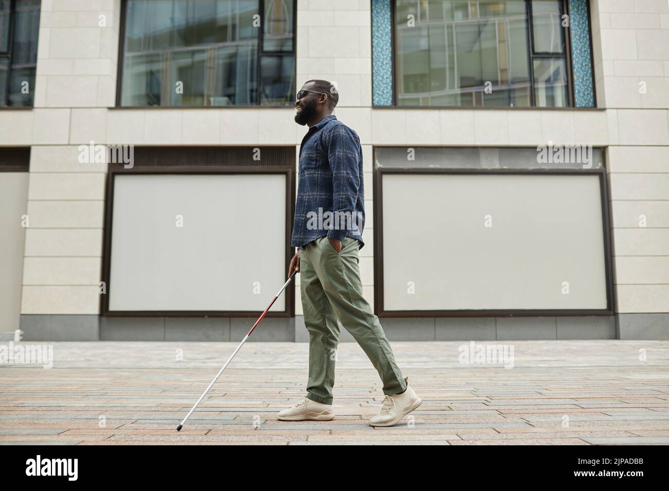 Full length portrait of smiling blind man walking in city and using cane, copy space Stock Photo