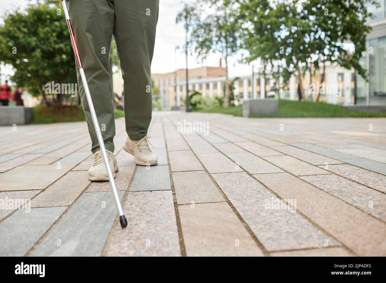 Low angle shot of blind man walking in city and using cane on pavement, copy space Stock Photo