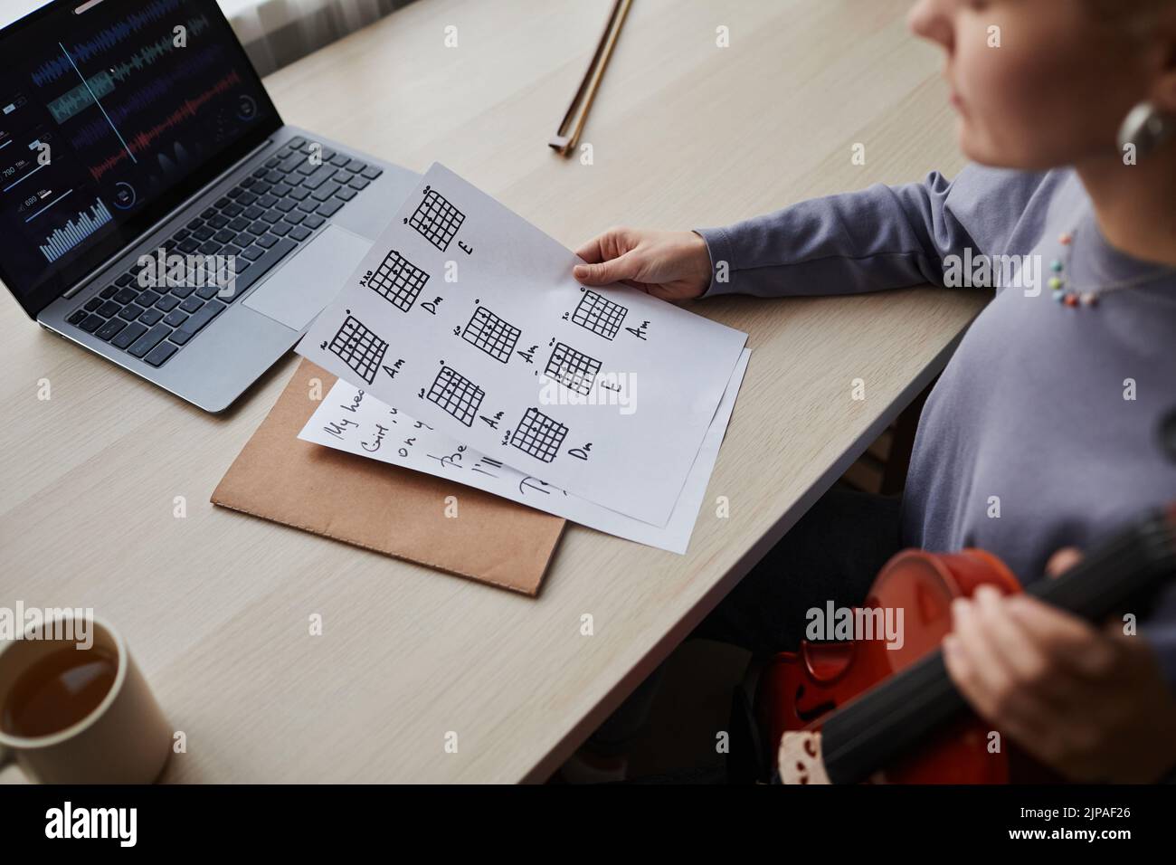 Close up of young woman holding music sheet while composing at home with violin Stock Photo