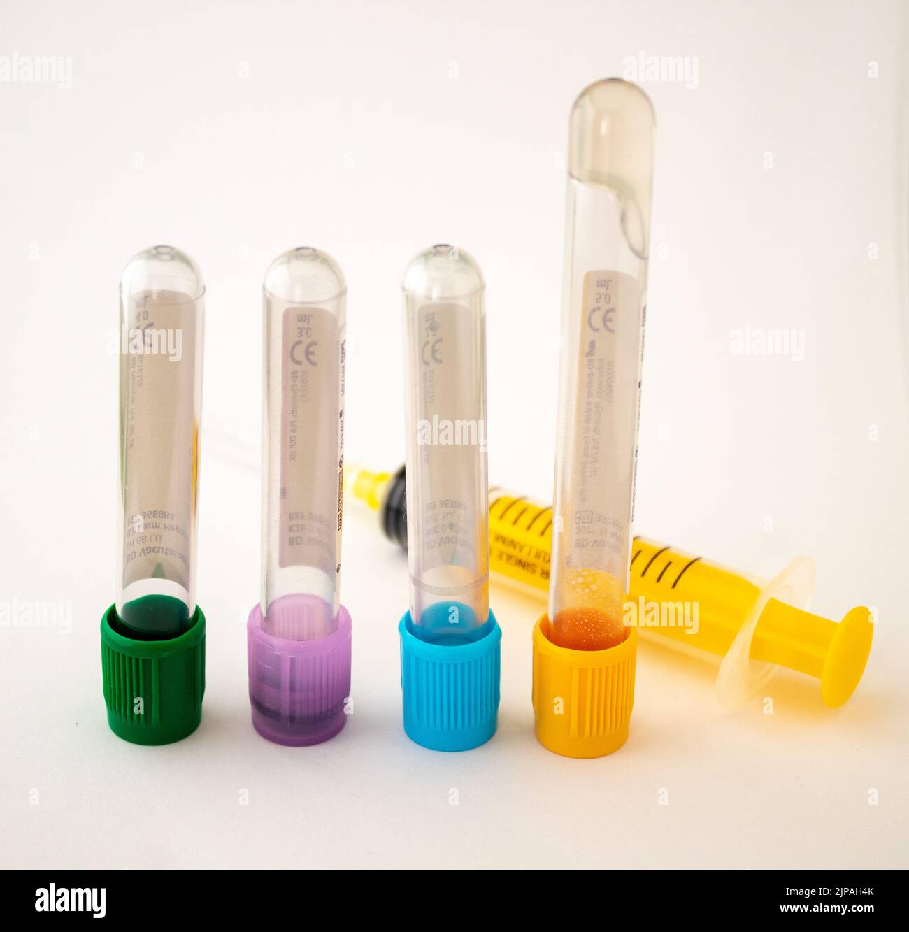 4 different colored blood test tubes with a yellow colored syringe on