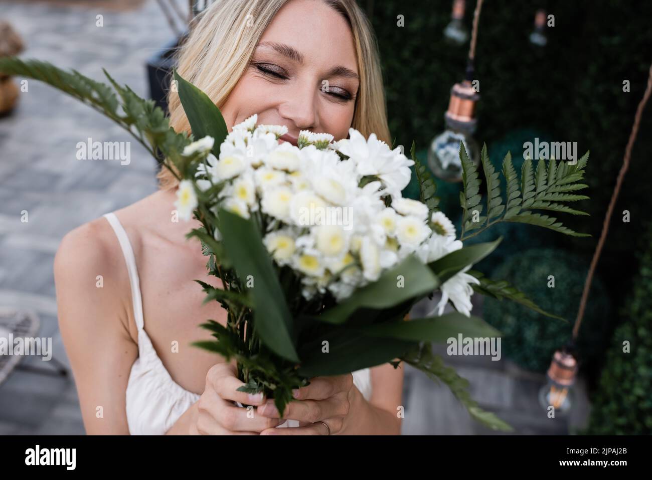 Blonde bride covering face with blurred bouquet on terrace Stock Photo ...