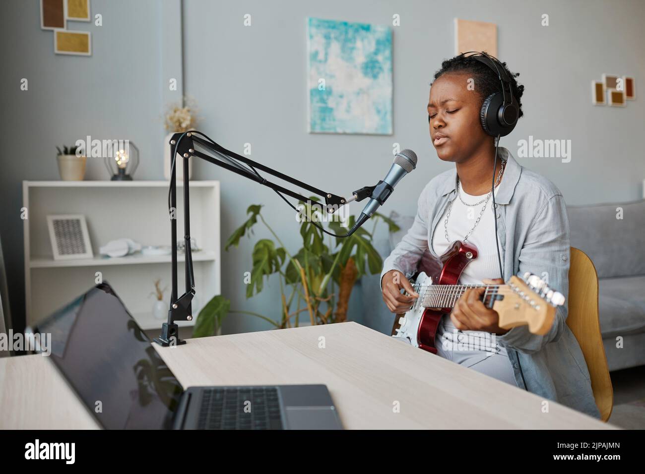 Minimal portrait of young black woman singing to microphone and playing guitar at home recording studio, copy space Stock Photo
