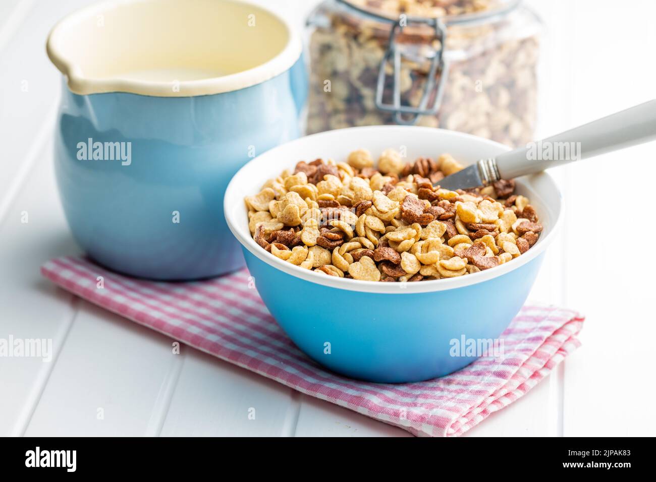 Breakfast cereal flakes in a bowl and milk on checkered napkin. Stock Photo