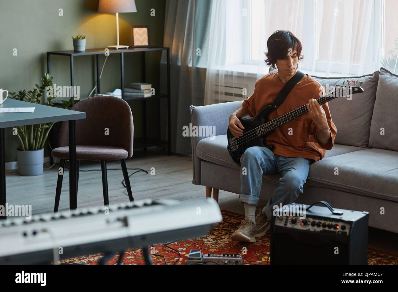 Full length portrait of young man playing electric guitar in cozy home music studio, copy space Stock Photo