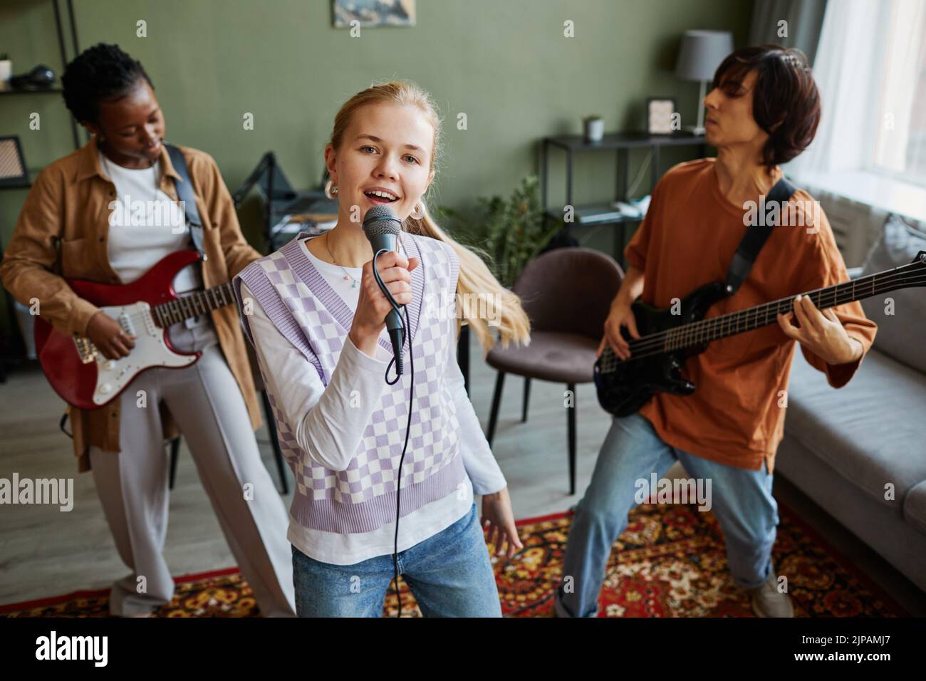 Portrait of music band practicing in home studio with focus on young blonde woman singing to microphone Stock Photo