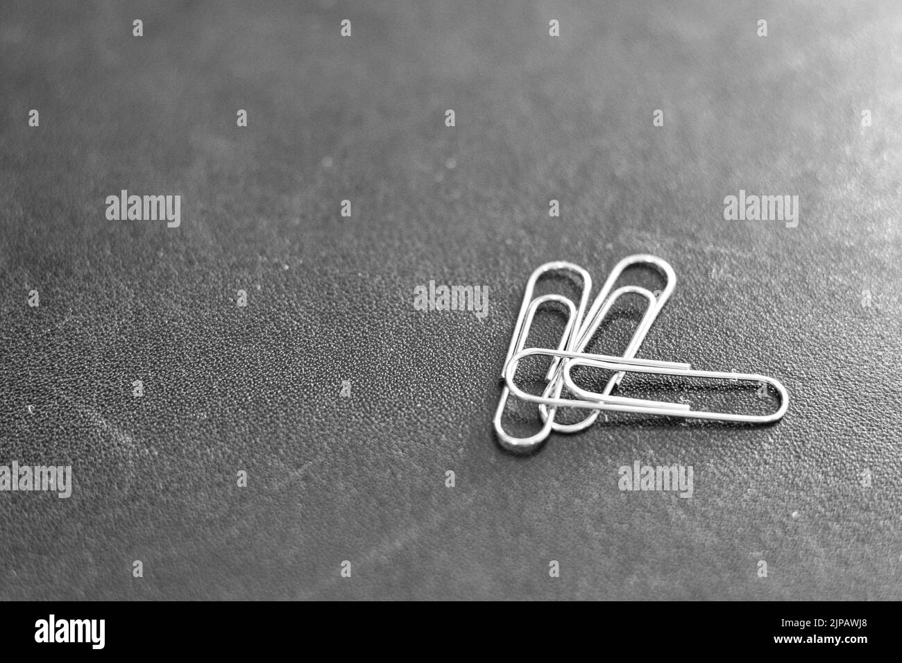 Three metal paperclips on a black leather surface Stock Photo Alamy