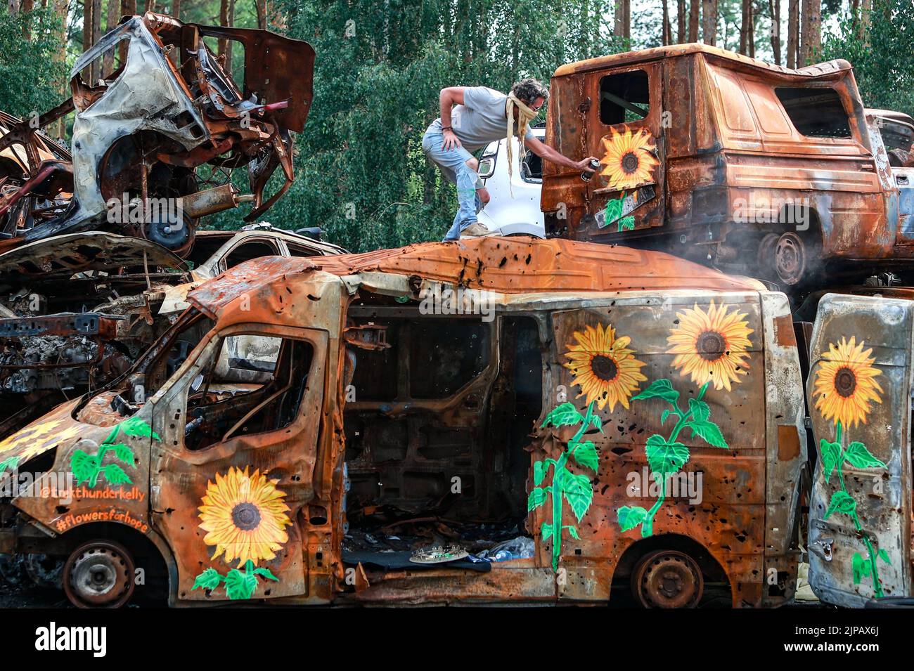 Irpin, Kyiv Oblast, Ukraine. 13th Aug, 2022. American visual artist TREK THUNDER KELLY, 53, based in Venice, California, paints sunflowers on a destroyed vehicle by Russian attacks, at a cemetery in Irpin, Kyiv Oblast, to raise money for Ukrainian people, amid the Russian invasion of Ukraine. Moscow continues to bear down on Ukraine with ferocity especially in Donetsk, Luhansk, Kharkiv and Kherson. (Credit Image: © Daniel Ceng Shou-Yi/ZUMA Press Wire) Stock Photo