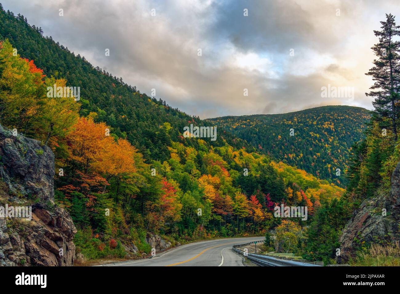 A two-lane highway winds through colorful autumn foliage at Crawford's Notch in New Hampshire's White Mountains. Stock Photo