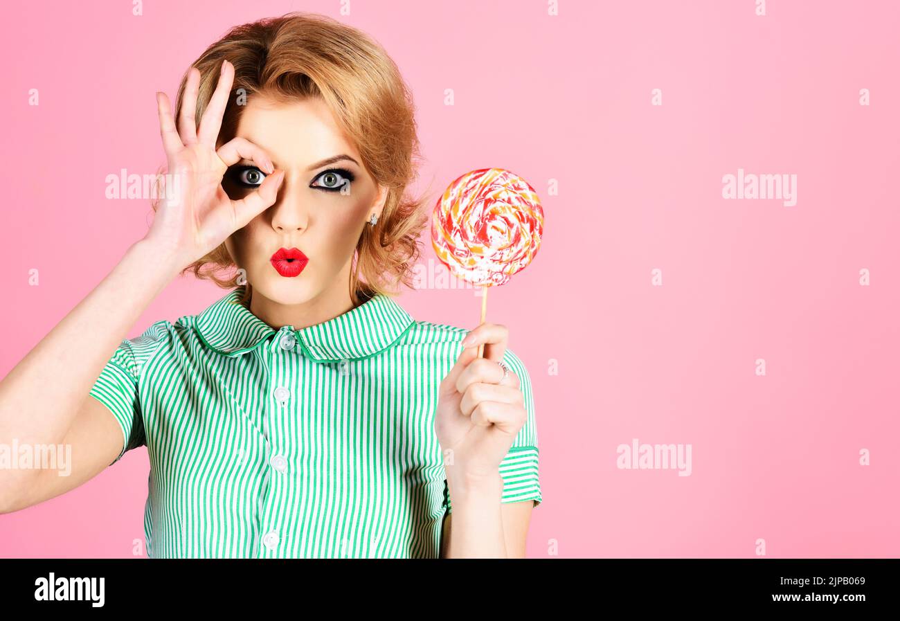 Beautiful girl with lollipop shows sign ok. Woman in summer style with colourful candy. Sweet food. Stock Photo