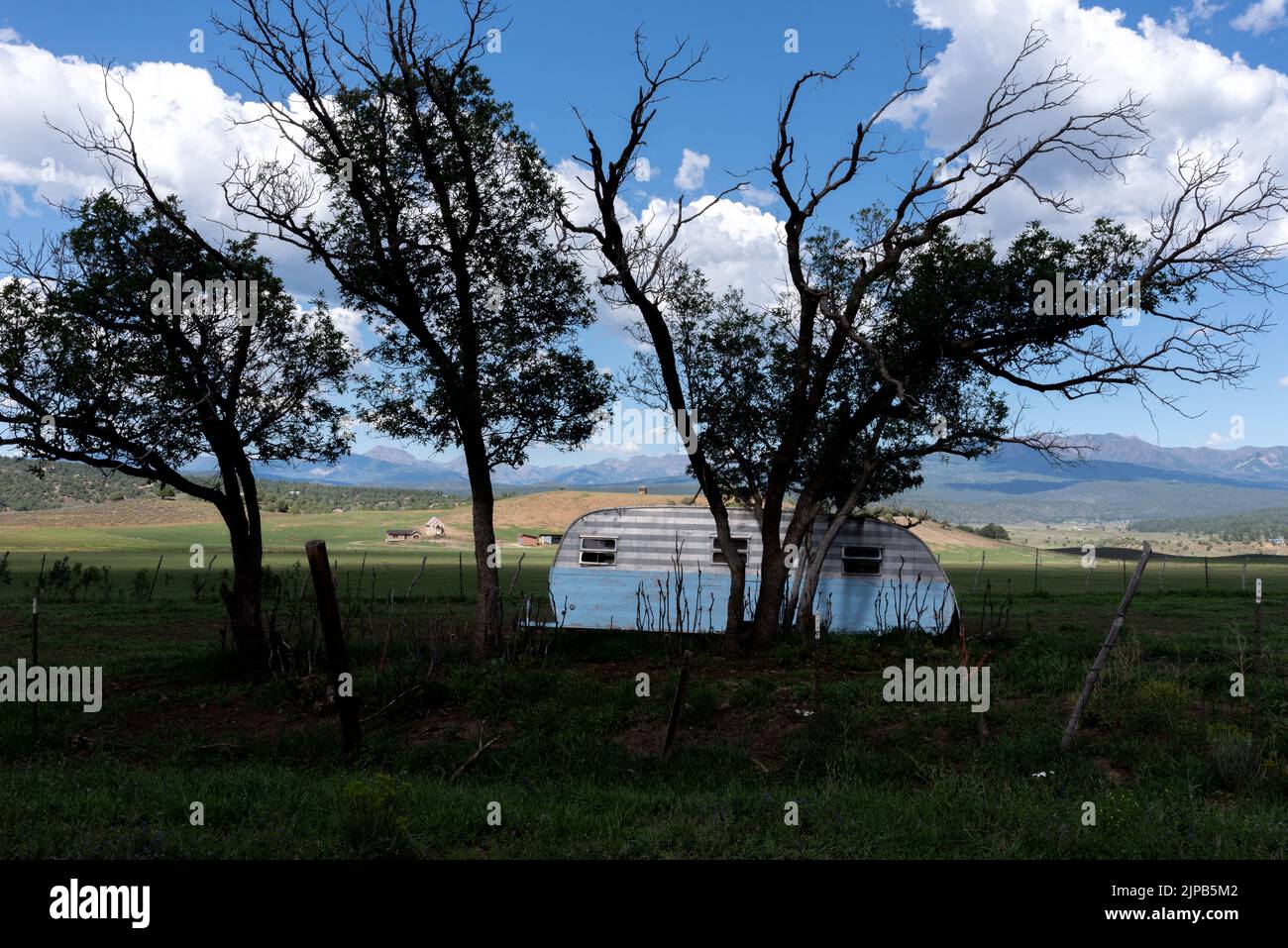 Silhouetted grassland and trees with open ranch land and a few houses and the Rocky Mountains in the background. Stock Photo