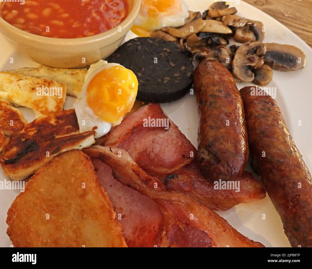 Full cooked British breakfast, including pork sausages with nitrites, cured bacon, egg, black pudding, mushrooms, Halloumi Stock Photo