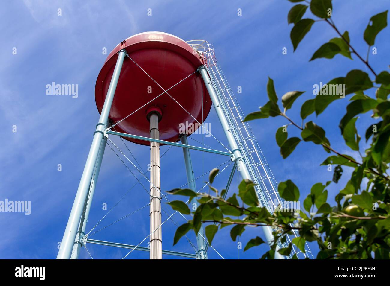 Upward view of a red and white round shaped water tower that resembles a fishing bobber, with blue sky background Stock Photo