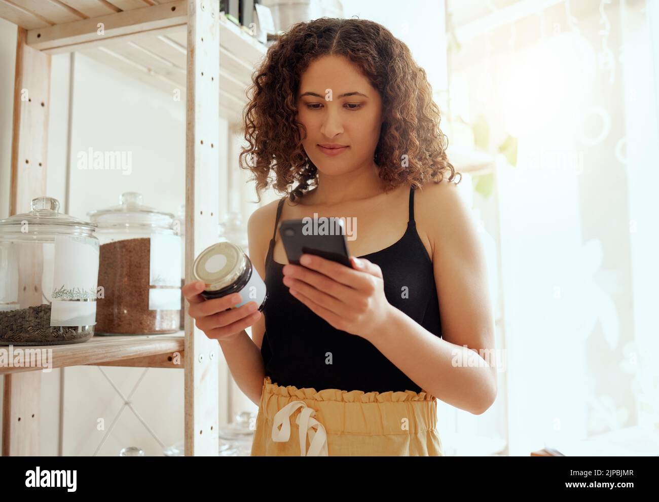 Female consumer or customer with phone searching organic product information online for ethical, vegan or healthy ingredients. Eco conscious buyer Stock Photo