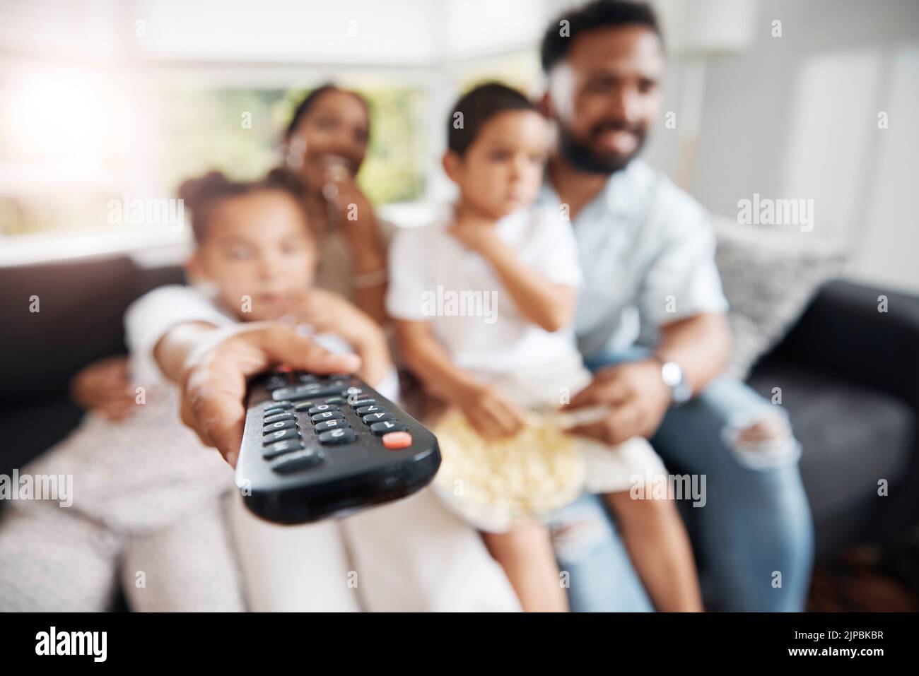 Closeup of remote control with family watching tv in their living room together. Parents and kids relaxing on the sofa enjoying a movie, series or Stock Photo