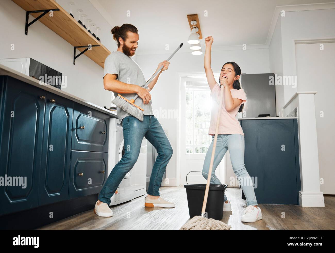 Having fun doing chores, dancing and singing father and daughter cleaning the living room together at home. Carefree, happy and cheerful parent Stock Photo
