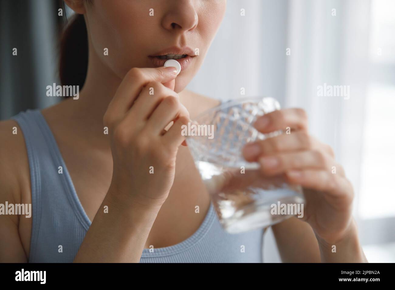 A young woman takes medications or vitamins. She's holding a glass of water. Stock Photo