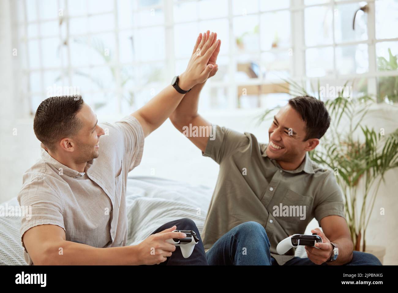 Men high five, celebrate and enjoy playing video games in the sofa at