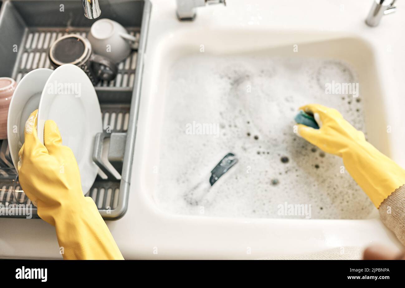 Housewife, maid or cleaner hands washing dishes in the kitchen sink for home hygiene, wearing rubber gloves. Contact us for cleaning solutions or Stock Photo