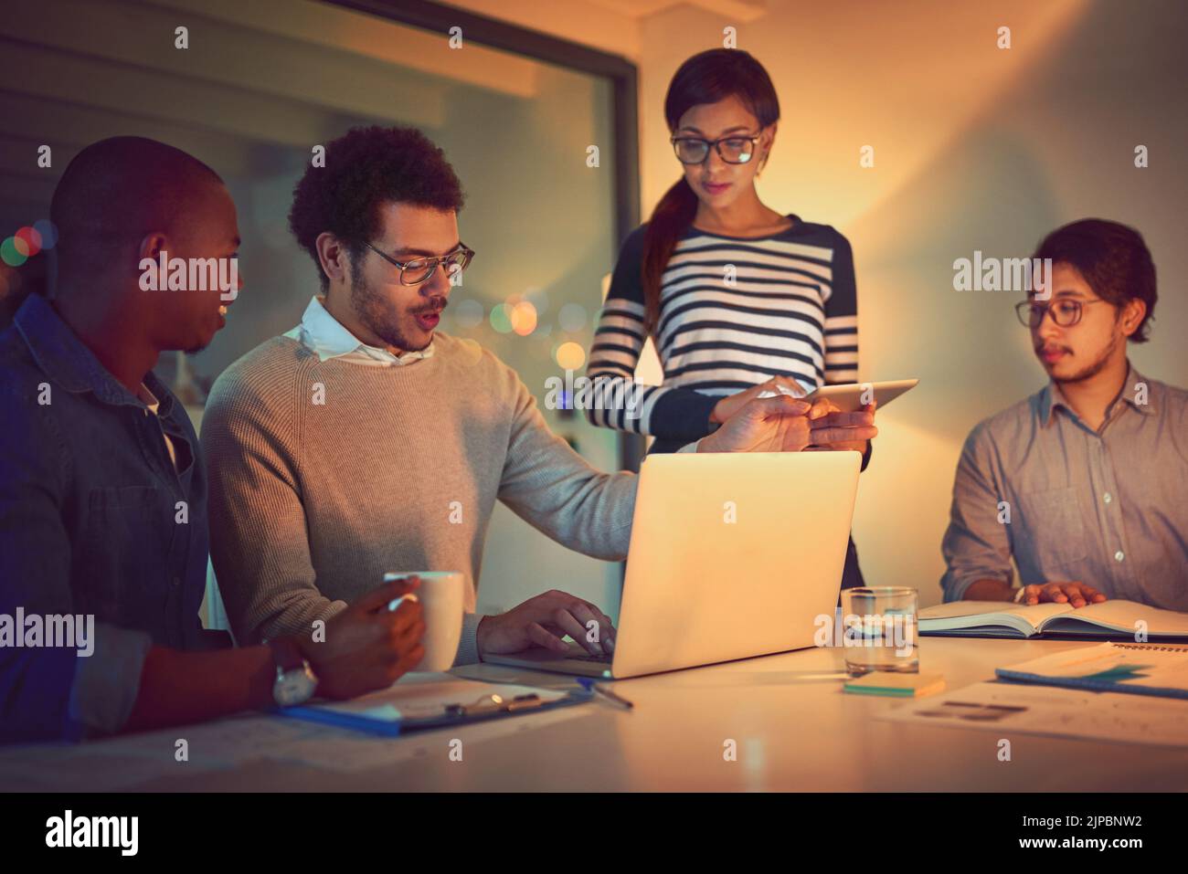 Making full use of the extra hours they have. a group of designers working late in an office. Stock Photo