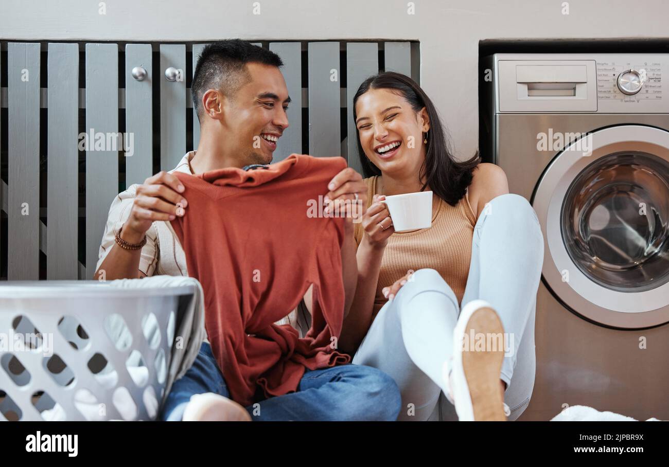 Carefree and funny couple doing laundry and relaxing together at home in the morning. Silly, goofy and playful lovers laughing and giggling while Stock Photo