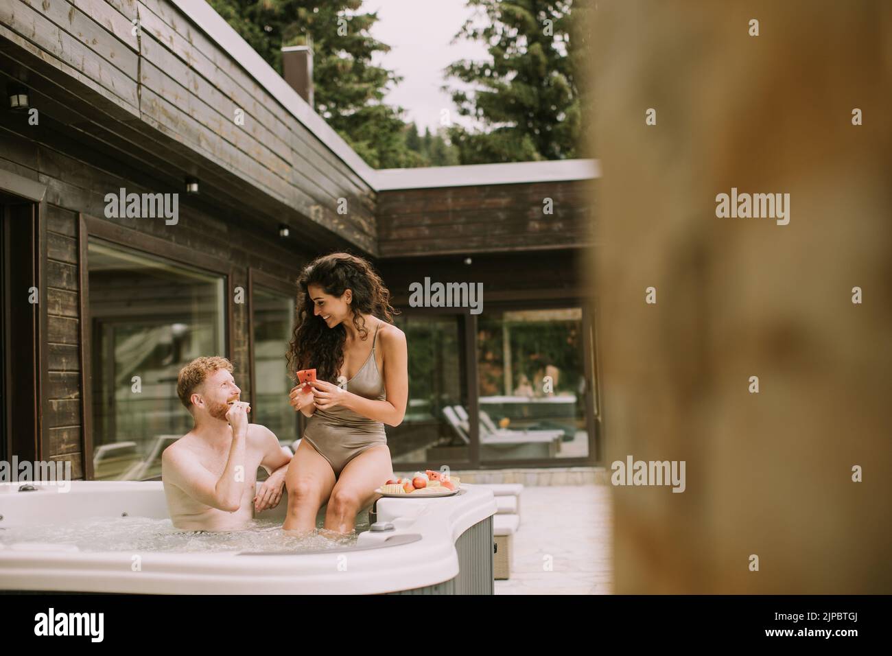 Attractive young couple enjoying in outdoor hot tub on vacation and eating fresh fruits Stock Photo