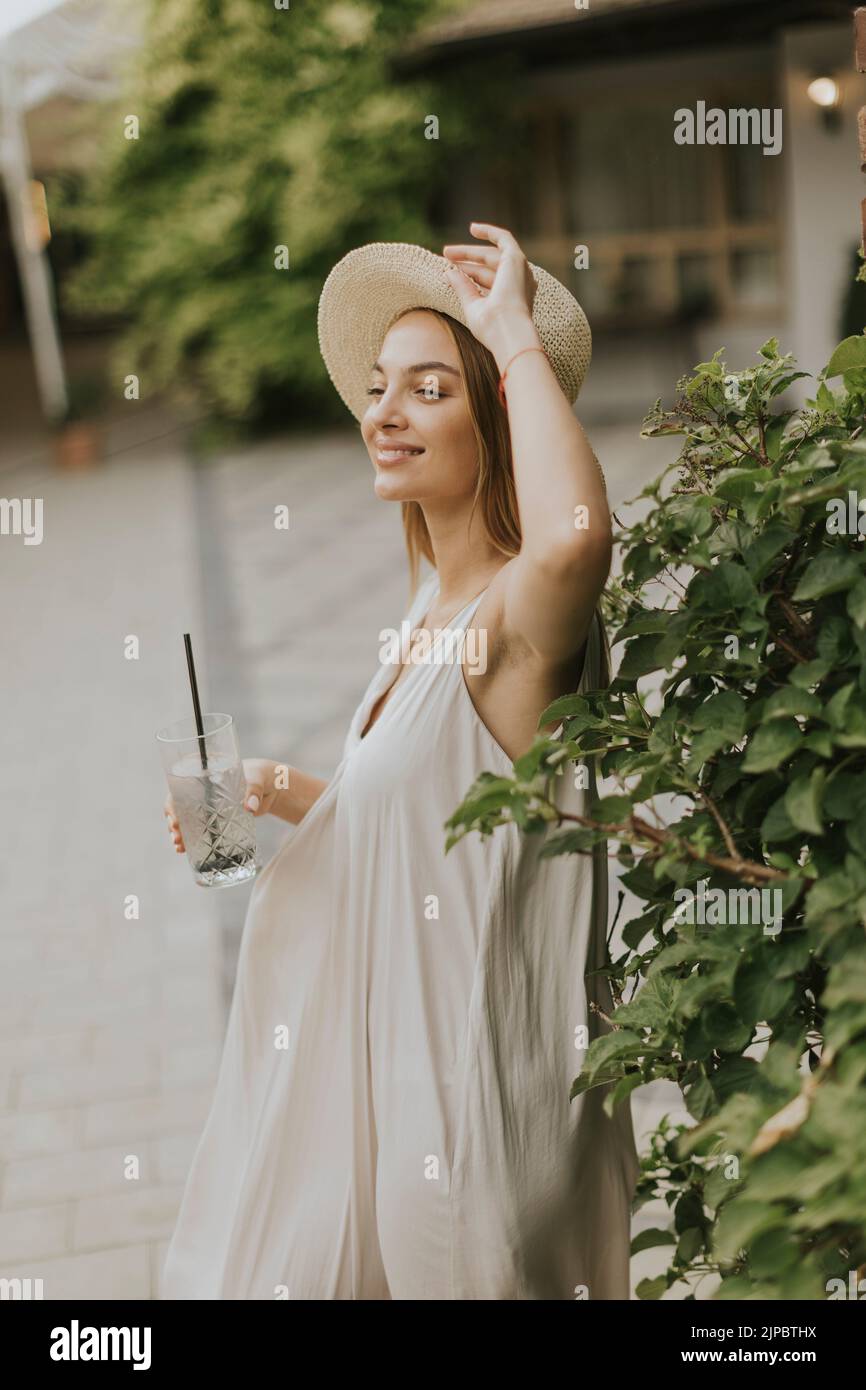 Pretty young woman with hat drinking cold lemonade in the resort garden Stock Photo