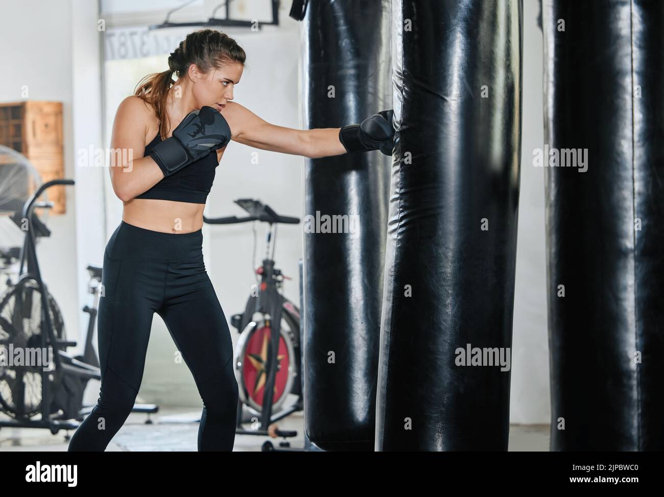 Young, active and strong female boxer punching a boxing bag in the gym to train for a match. Healthy athlete doing a kickboxing workout. Fit Stock Photo