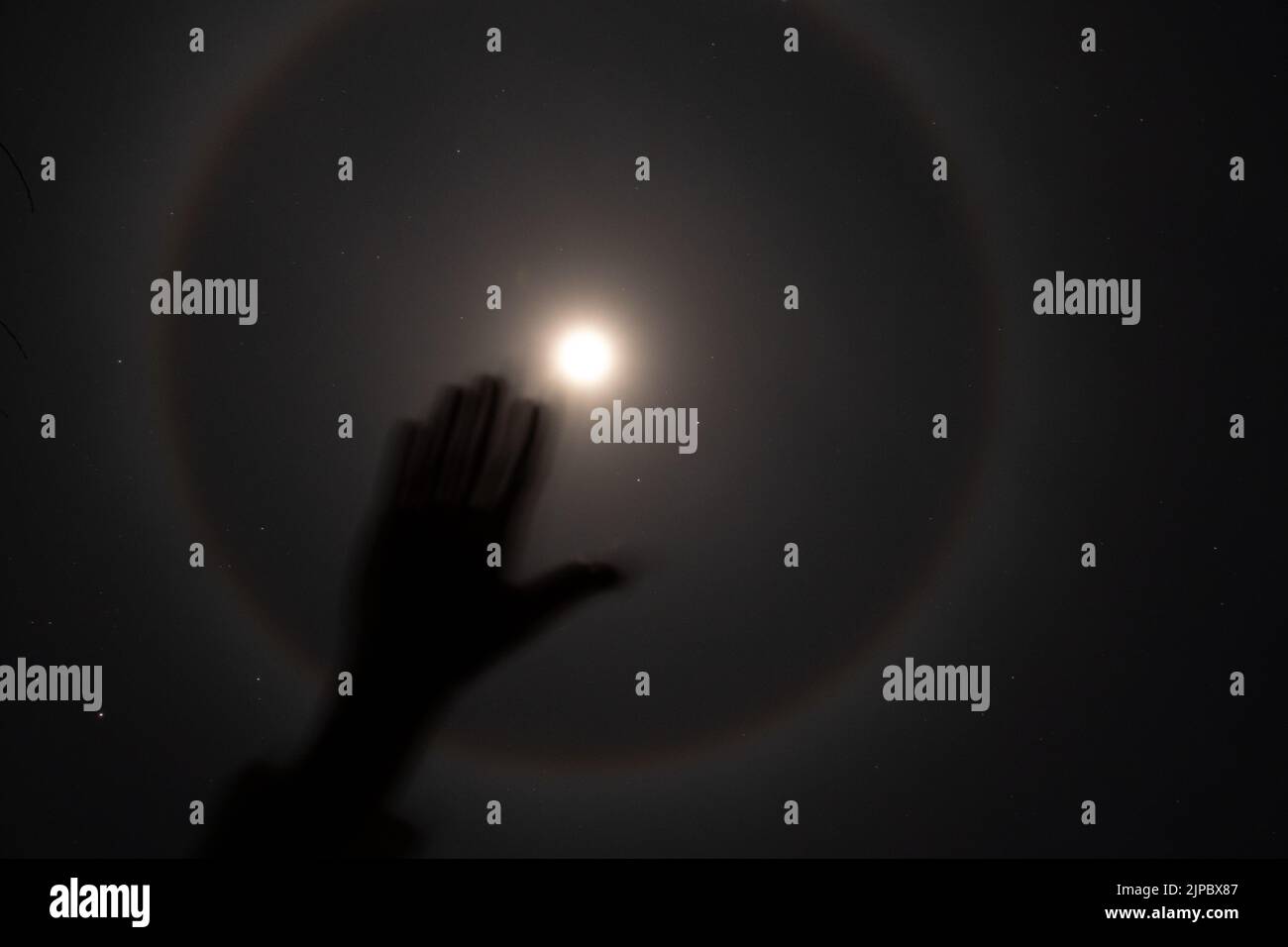 The halo phenomenon on the moon over Ukraine at night and the girl's hand 2022, the night moon and stars as a background Stock Photo