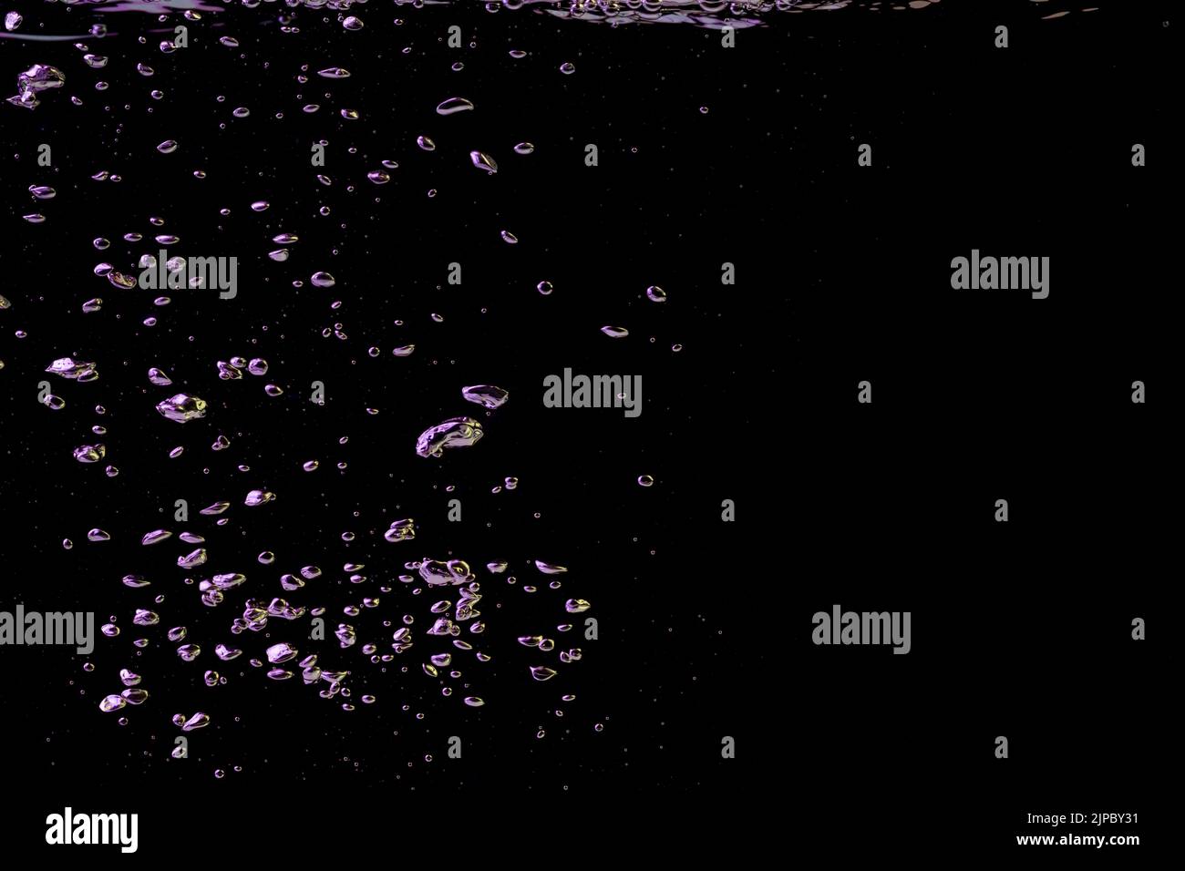 A bubble splash in transparent clear water liquid in yellow and purple light on a black nature background Stock Photo