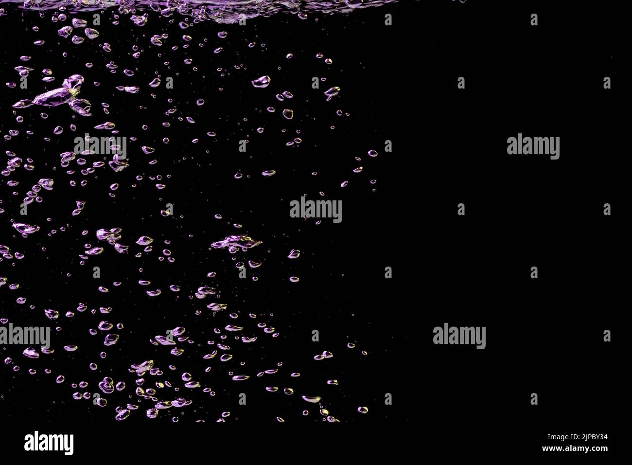 A bubble splash in transparent clear water liquid in yellow and purple light on a black nature background Stock Photo