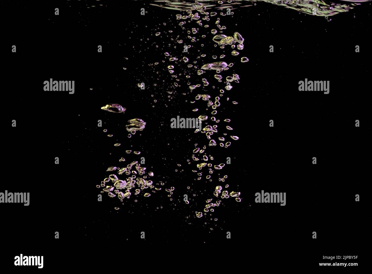 A bubble splash in transparent clear water liquid in yellow and purple light on a black nature background Stock Photo