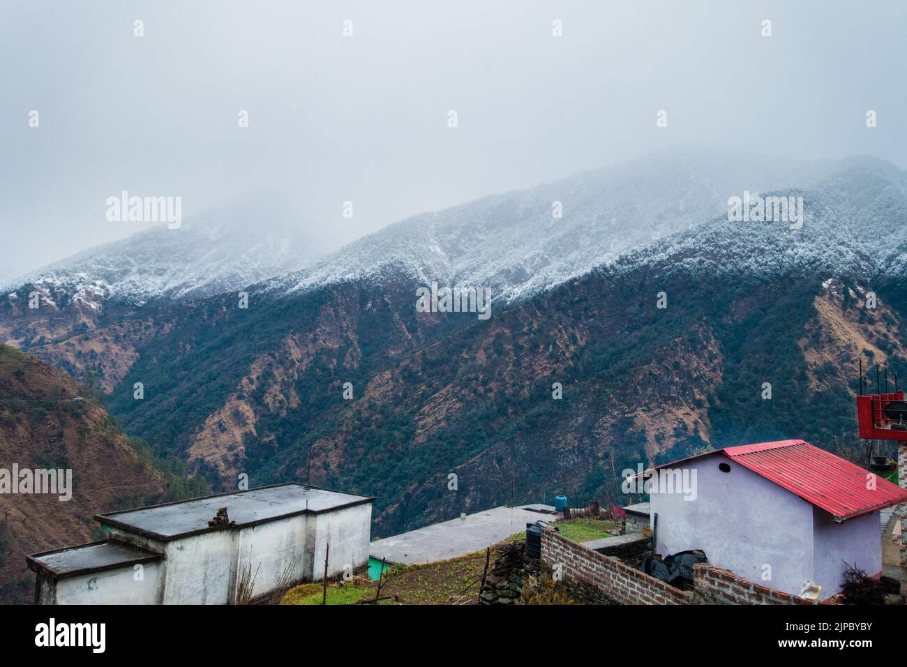 Uttarakhand. India. 23rd Jan2022.A beautiful shot village homes with snow covered mountains of himalayas in the Okhimath district of Chamoli garhwal. Stock Photo