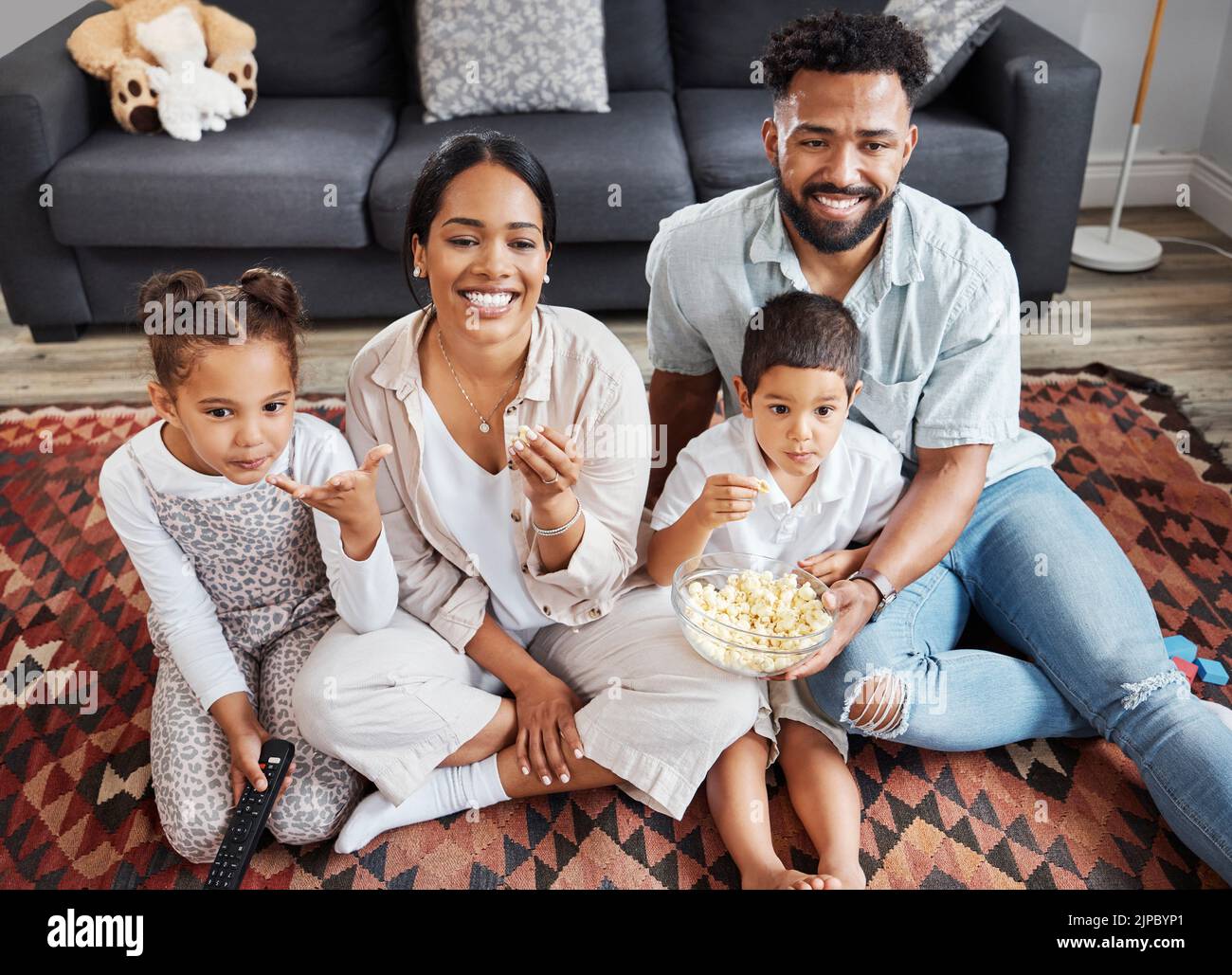 Watching movie, family bonding and eating popcorn while relaxing in the lounge together at home. Happy, smiling and carefree parents enjoying snack Stock Photo