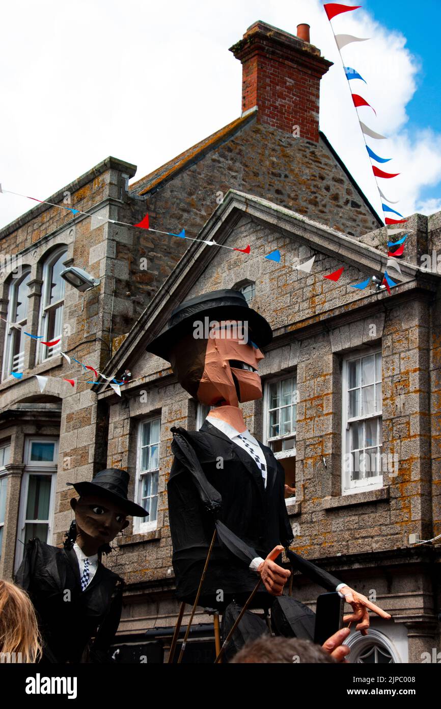Giant papier mache figures process down the street in Penzance for