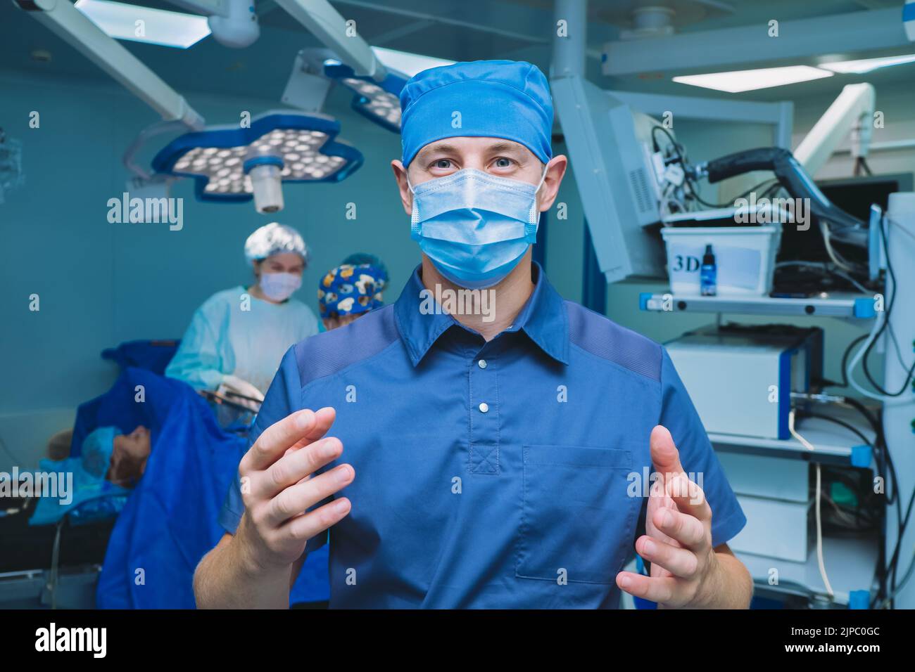 A male surgeon holds sanitized hands in front of him in an operating