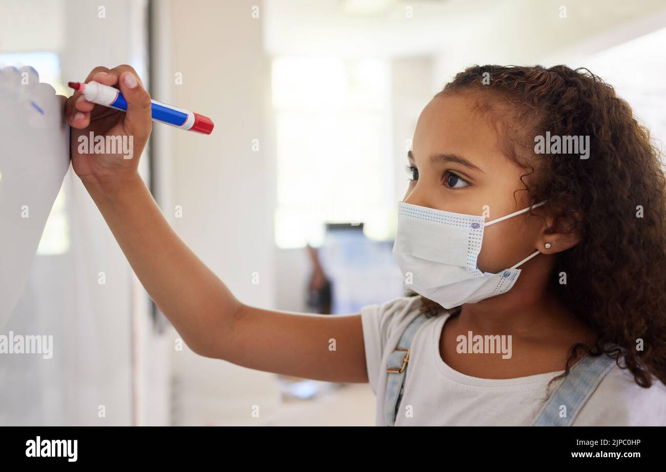 School student writing on whiteboard in class during covid pandemic for learning, education and study. Young kindergarten, preschool or elementary kid Stock Photo