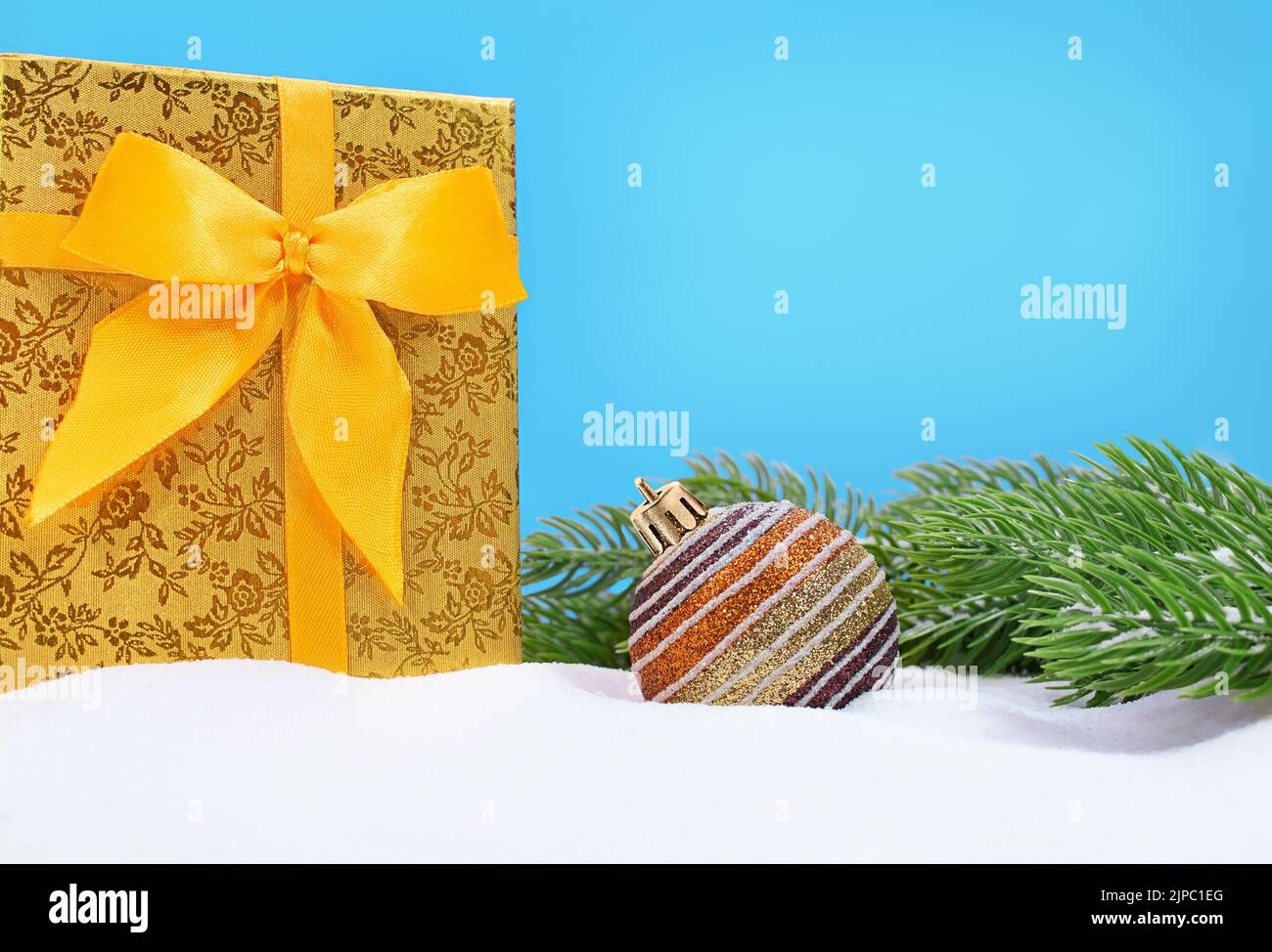 Big yellow gift box with bow and shiny ball and fir branches on snow. Christmas, New Year. Copy space Stock Photo