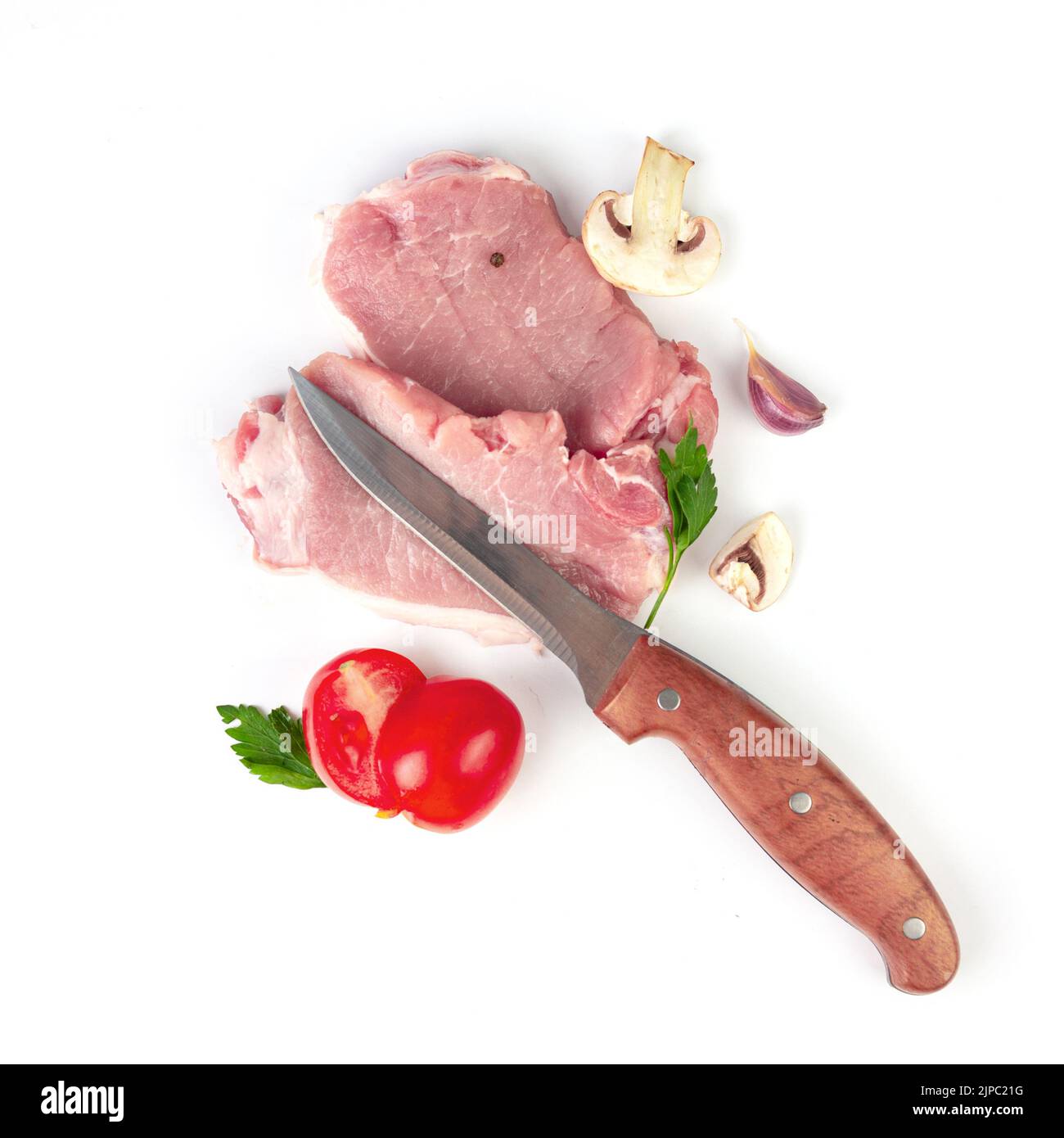 Fresh raw meat with herbs, spices, garlic, tomato, spice, pepper, champignon and butcher knife on white background. Stock Photo