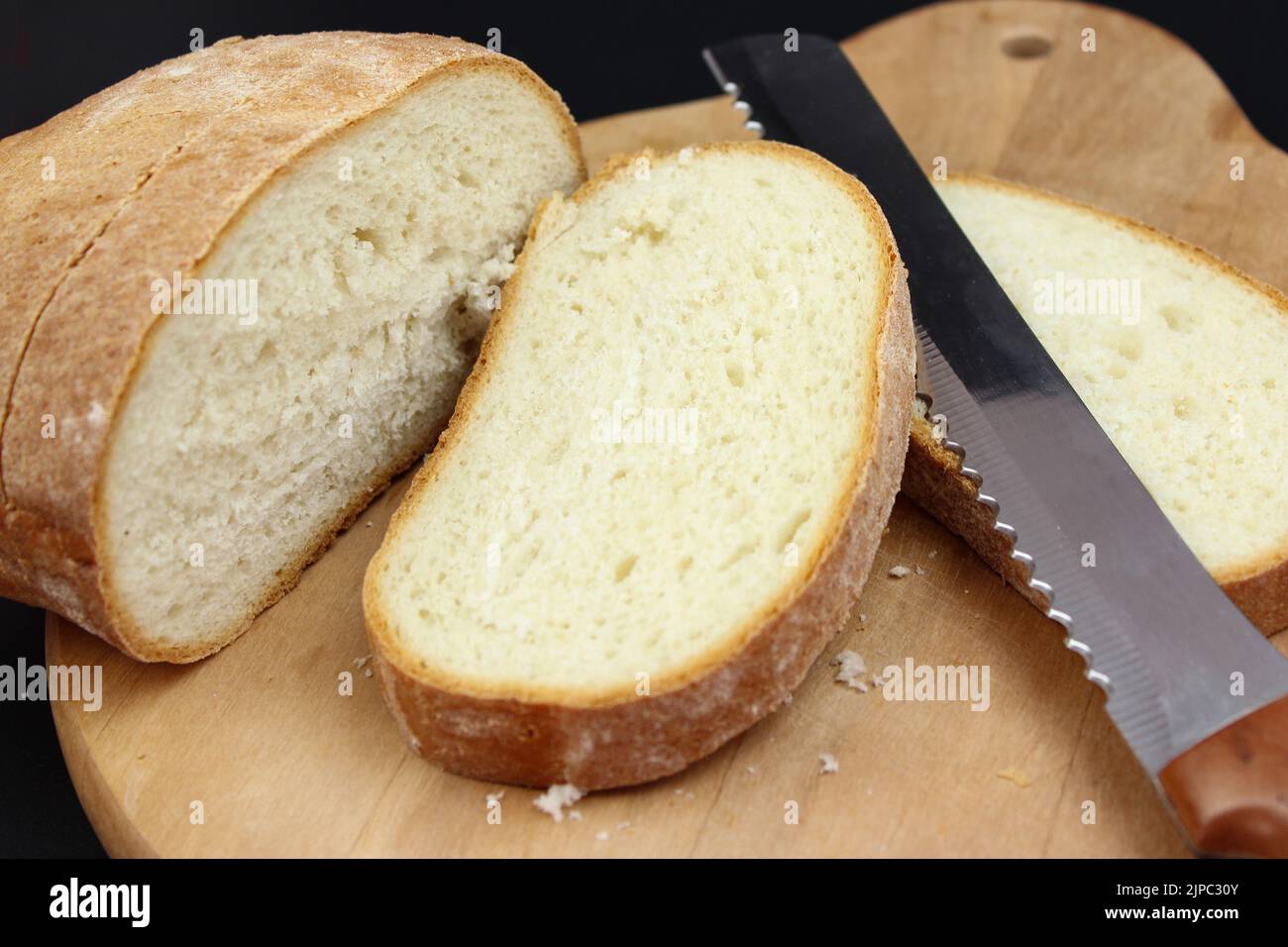 Wooden cutting board with sliced white bread and knife on black background Stock Photo