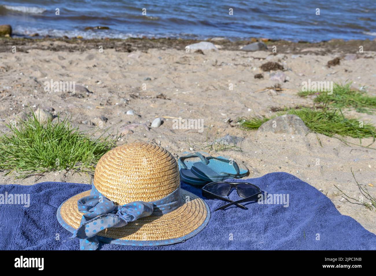 Straw hat, sunglasses and flip-flops on a blue towel on a natural beach ...