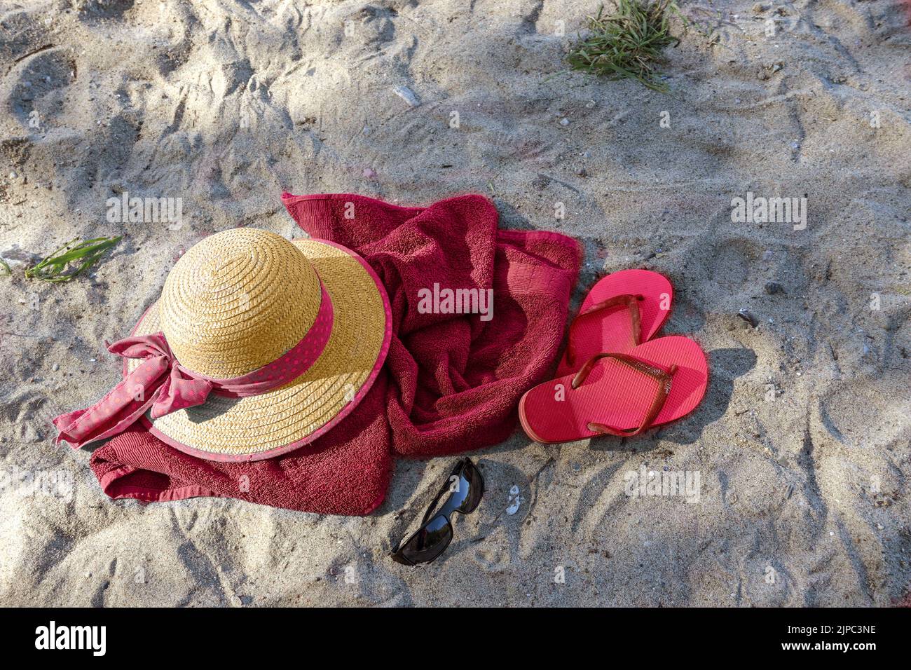 Summer beach vacations, straw hat and flip flops on a red towel in the sand near the tourist resort Boltenhagen, Baltic Sea, Germany, copy space, view Stock Photo